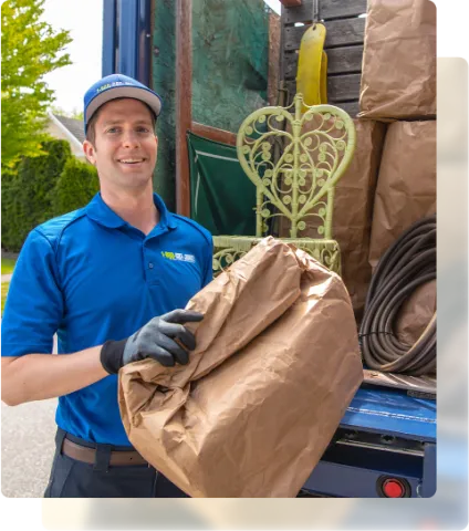 1-800-GOT-JUNK? employee posing by junk removal truck holding brown paper bag